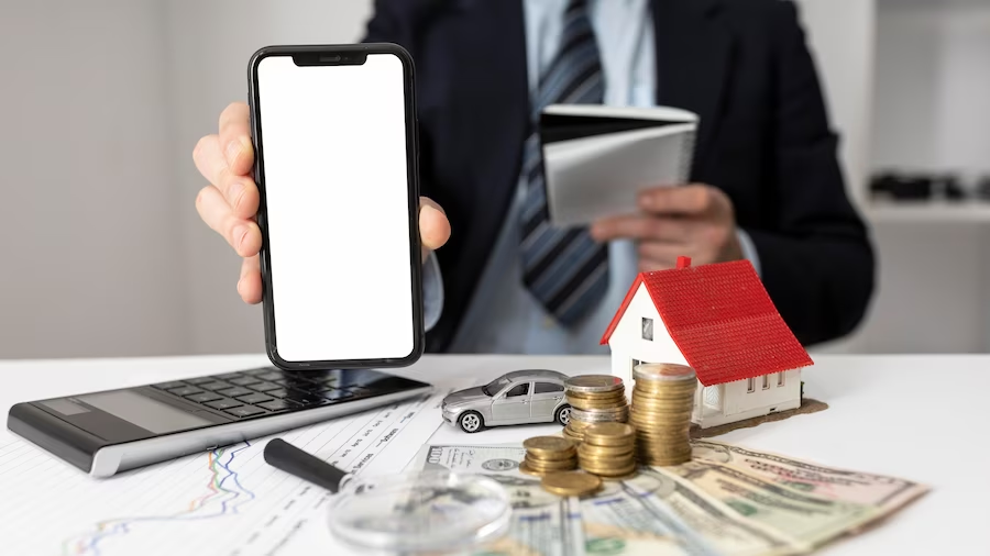 a hand showing a white screen mobile with money car and house models
